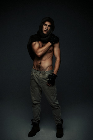 Young fashion topless man in knitted scarf on his had isolated on dark backgroundの写真素材