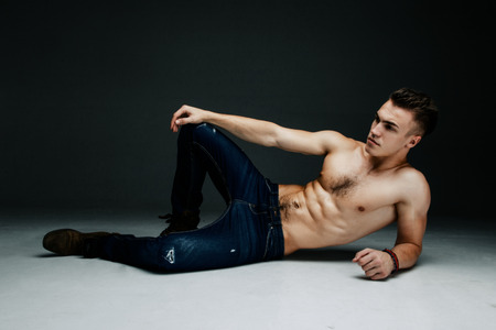 Young fashion topless man lying on the floor isolated on dark background. Strong Athletic Man Fitness Model Torso showing six pack absの写真素材