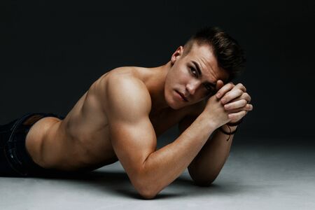 Portrait of a handsome topless man inflated lying on the floor on dark backgroundの写真素材