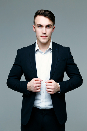 Handsome stylish man in elegant black suit and black pants on gray backgroundの写真素材