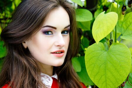 Gorgeous young woman in red dress on green trees backgroundの写真素材