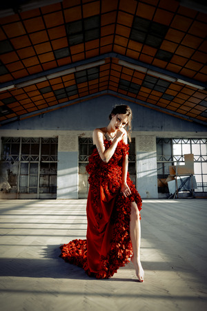 Beautiful, brunette woman in an old, abandoned house, wearing a red dress,の写真素材