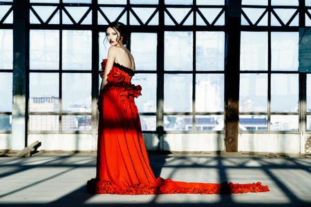 Beautiful, brunette woman in an old, abandoned house, wearing a red dress,の写真素材