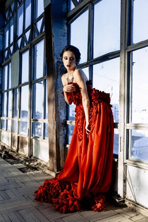 Beautiful, brunette woman in an old, abandoned house, wearing a red dress,の写真素材