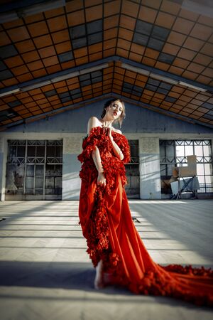 Beautiful, brunette woman in an old, abandoned house, wearing a red dress,の写真素材