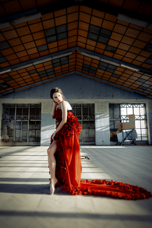 Beautiful, brunette woman in an old, abandoned house, wearing a red dress,の写真素材