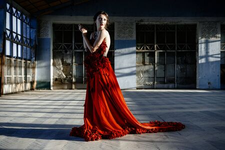Beautiful, brunette woman in an old, abandoned house, wearing a red dress,の写真素材
