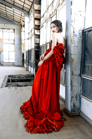 Beautiful, brunette woman in an old, abandoned house, wearing a red dress,の写真素材