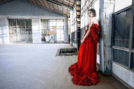 Beautiful, brunette woman in an old, abandoned house, wearing a red dress,の写真素材