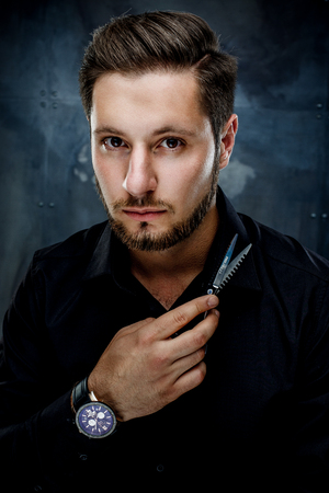 Elegant young handsome man. Studio fashion portrait.Man holding scissors and provocatively looking at cameraの写真素材