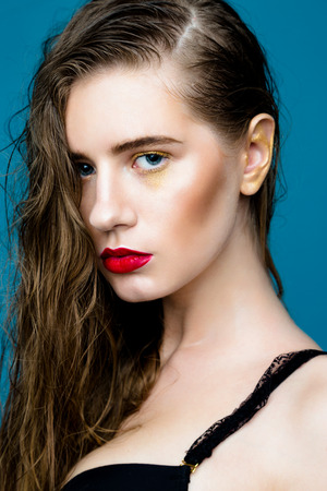 Beauty fashion girl. Portrait of beautiful young woman with fresh clean skin and red lips on blue backgroundの写真素材
