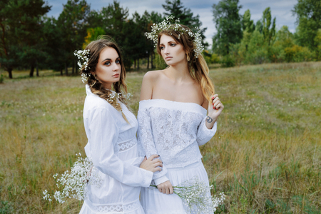 Two women in white dresses with flowers outdoorsの写真素材