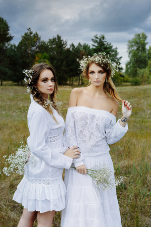 Two women in white dresses with flowers outdoorsの写真素材