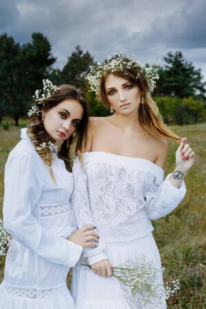 Two women in white dresses with flowers outdoorsの写真素材