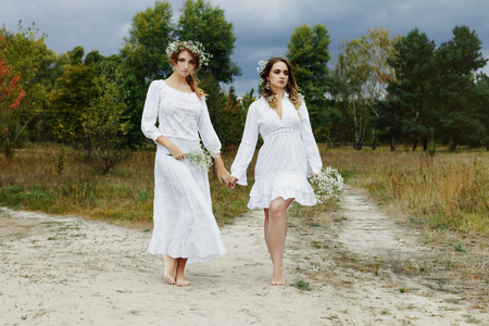 Two women in white dresses with flowers outdoorsの写真素材