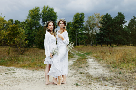 Two women in white dresses with flowers outdoorsの写真素材