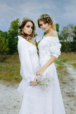 Two women in white dresses with flowers outdoorsの写真素材
