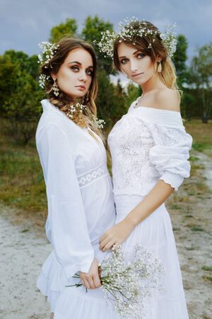 Two women in white dresses with flowers outdoorsの写真素材