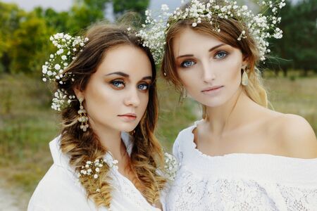 Two women in white dresses with flowers outdoorsの写真素材