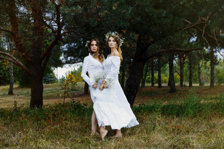 Two women in white dresses with flowers outdoorsの写真素材