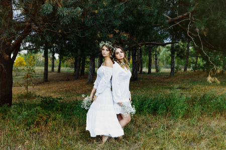 Two women in white dresses with flowers outdoorsの写真素材