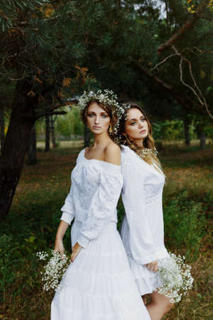 Two women in white dresses with flowers outdoorsの写真素材