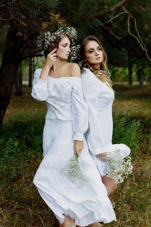 Two women in white dresses with flowers outdoorsの写真素材