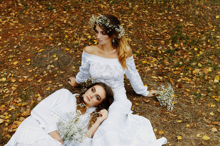 Two women in white dresses with flowers outdoorsの写真素材