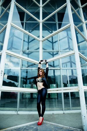 Beautiful young woman posing on street over glass wall backgroundの写真素材