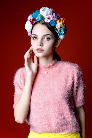 Beautiful model with a wreath of flowers on her head on red backgroundの写真素材