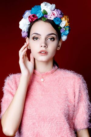 Beautiful model with a wreath of flowers on her head on red backgroundの写真素材