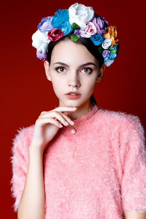 Beautiful model with a wreath of flowers on her head on red backgroundの写真素材