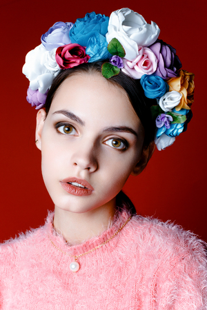 Beautiful model with a wreath of flowers on her head on red backgroundの写真素材