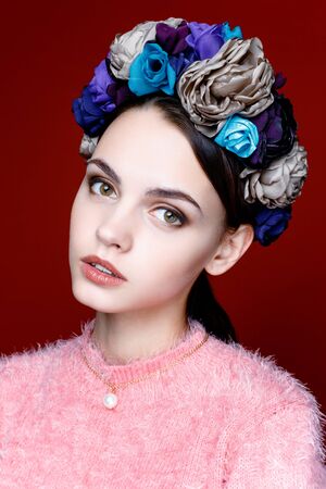 Beautiful model with a wreath of flowers on her head on red backgroundの写真素材
