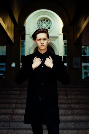 handsome young man in black coat outdoors on building backgroundの写真素材