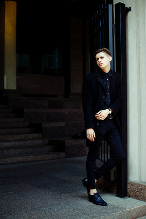 handsome young man in black coat outdoors on building backgroundの写真素材