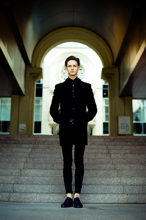 handsome young man in black coat outdoors on building backgroundの写真素材