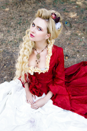 Blonde woman with long curly hair with flower accessory in antique red dressの写真素材