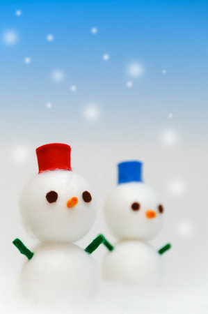 Snowman family on blue background with snowflakes and bokehの写真素材