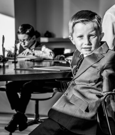 A boy wearing suit is sitting in an office looking at the camera