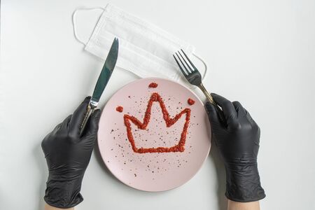 Protective mask and hands in black gloves hold a fork with a knife on a white background.の写真素材