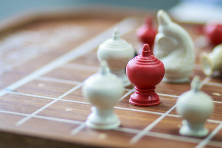 red pawn surrounded by black chess pieces on a chess boardの写真素材