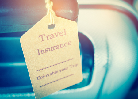 Travel Insurance tag on Suitcase safety with letters enjoyable your trip on bag light blurred backgroundの写真素材