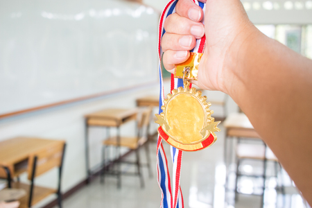 Students hands raised holding two gold medals with Thai ribbon against blur empty classroom at school greenboard background, Show success in studying, Winners success awards in educational concept.の写真素材