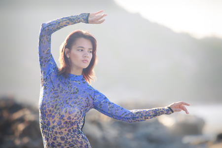 brunet gymnast girl sitting at a rock with bare legs and back in an acrobatic tights against seaの写真素材