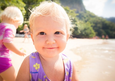 portrait of small blonde baby girl in purple swim suit play on seashore closeupの写真素材