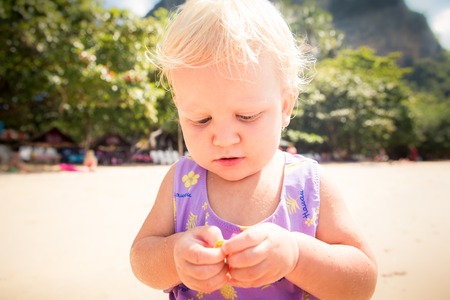 portrait of small blonde baby girl in purple swim suit play on seashore closeupの写真素材