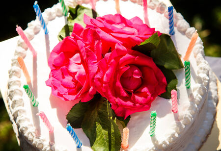 closeup white creamy delicious cake decorated with candles  and three red roses on the topの写真素材