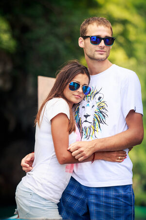 tall handsome man hold his pretty brunette girl wear sunglases and stand on longtail boatの写真素材
