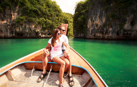 attractive brunette girl with her boyfriend sit on longtail boat in green lagoon among cliff islandの写真素材